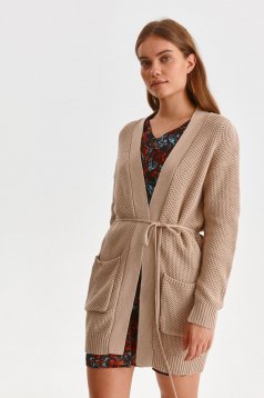 Cream cardigan knitted with pockets is fastened around the waist with a ribbon